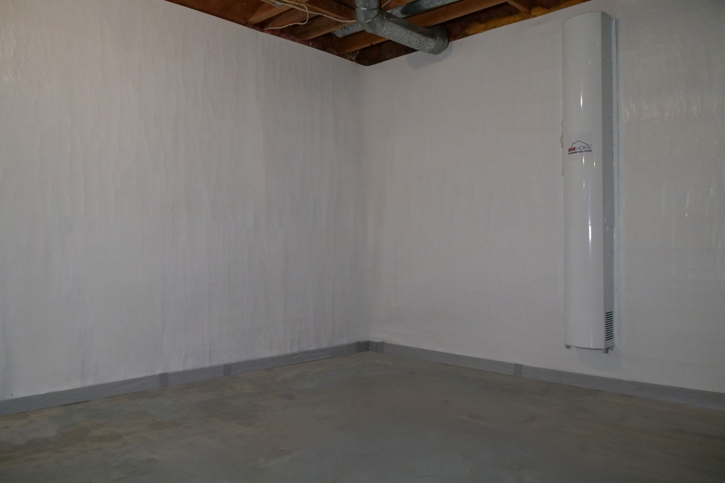 A completed Erie Home waterproofed basement with the clean white encapsulated walls and the air purification system hanging from the wall.