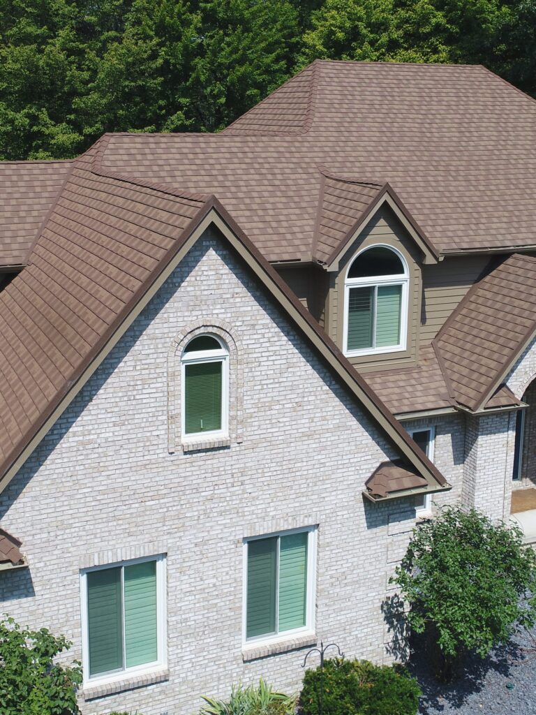 brown metal roof on a gray house in front of trees